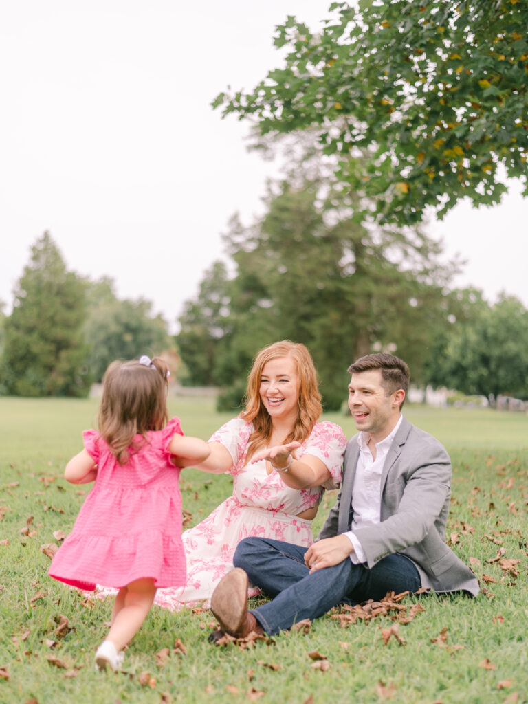 Little girl in pink dress running to Mom and Dads arms at park in Charlotte Hall, MD.