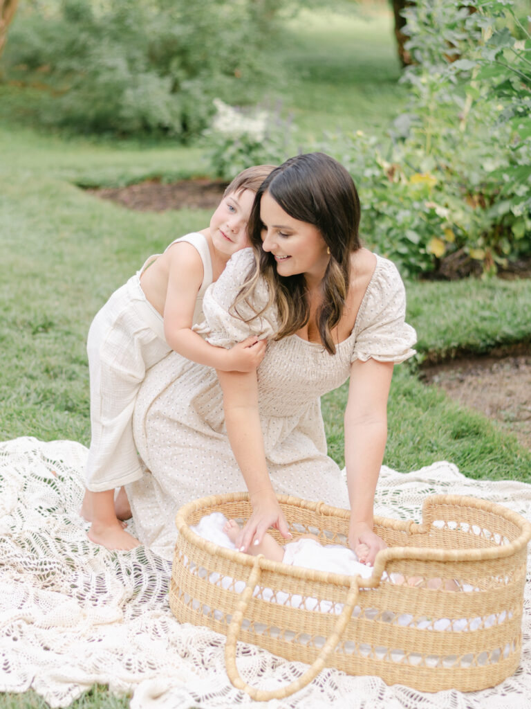 Little boy loving on mom while mom touches baby in moses basket at family photo session