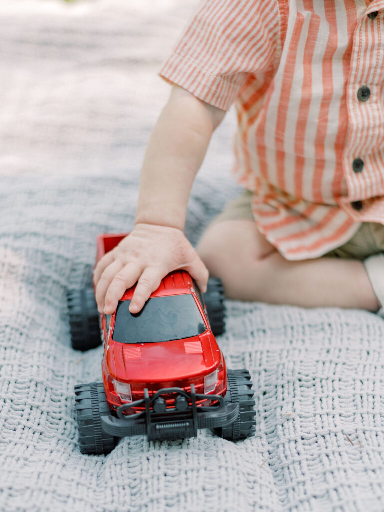 Little boys hand on red truck while playing on blanket at Pratt Park.