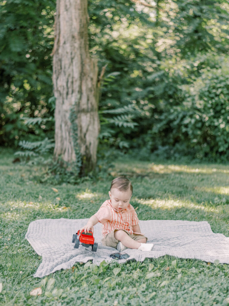 Boy sitting on blanket playing with his red truck.