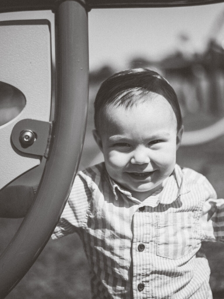 Black and white photo of young boy laughing while playing at a playground.