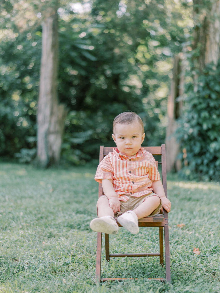 One year old boy with serious face sitting on antique wooden chair.