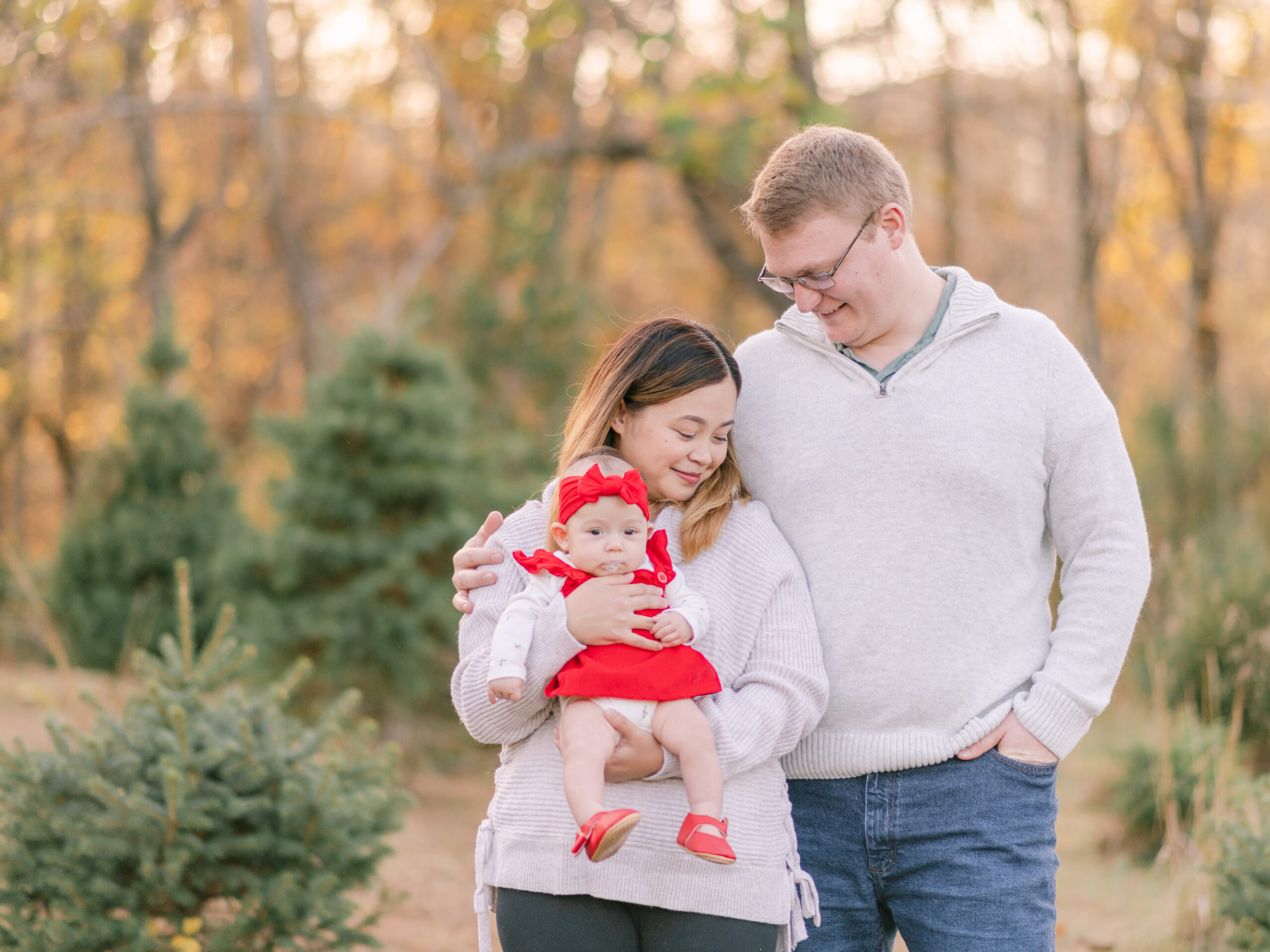 Mom and dad cuddling while holding little girl in red dress during family photos.