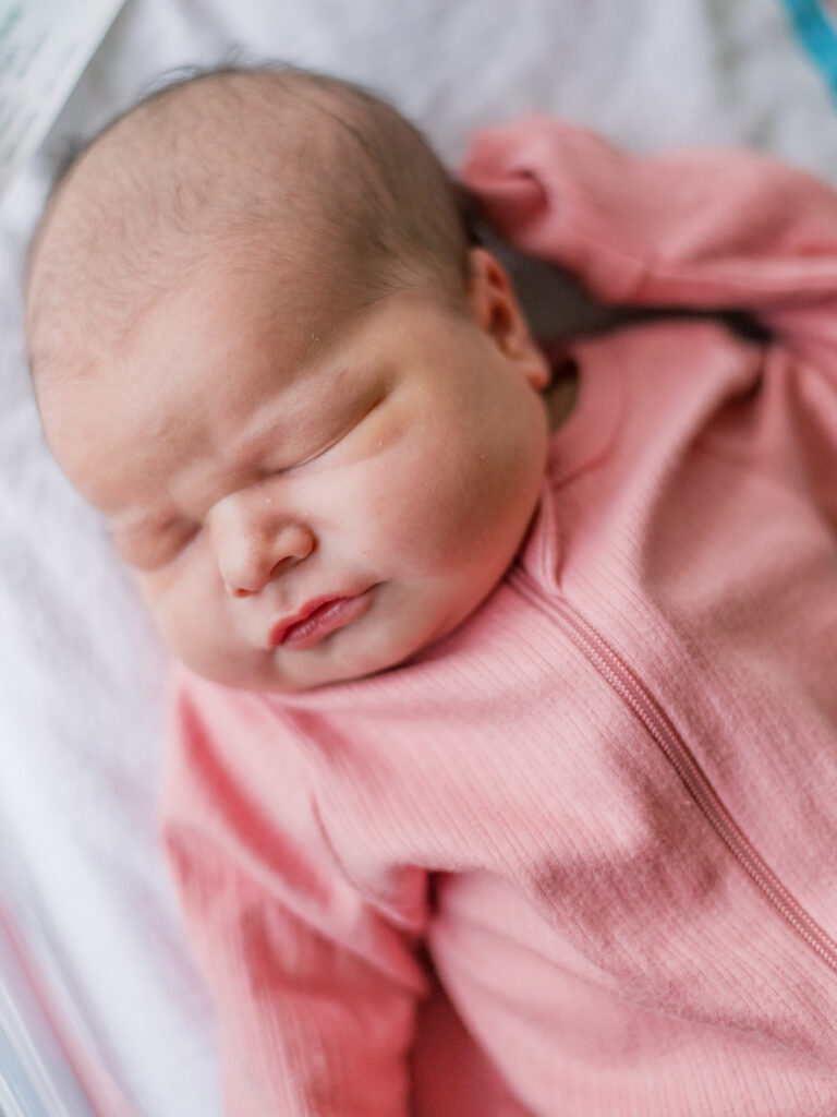 Newborn baby girl in pink sleeper during photo session with Shelby McKimmie Photography.