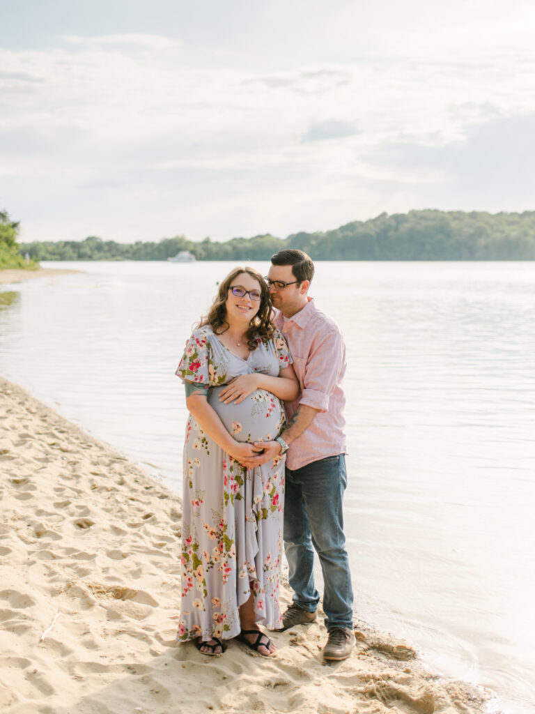 Mom holding her belly and dad embracing her during their beach Maternity Session in Maryland.