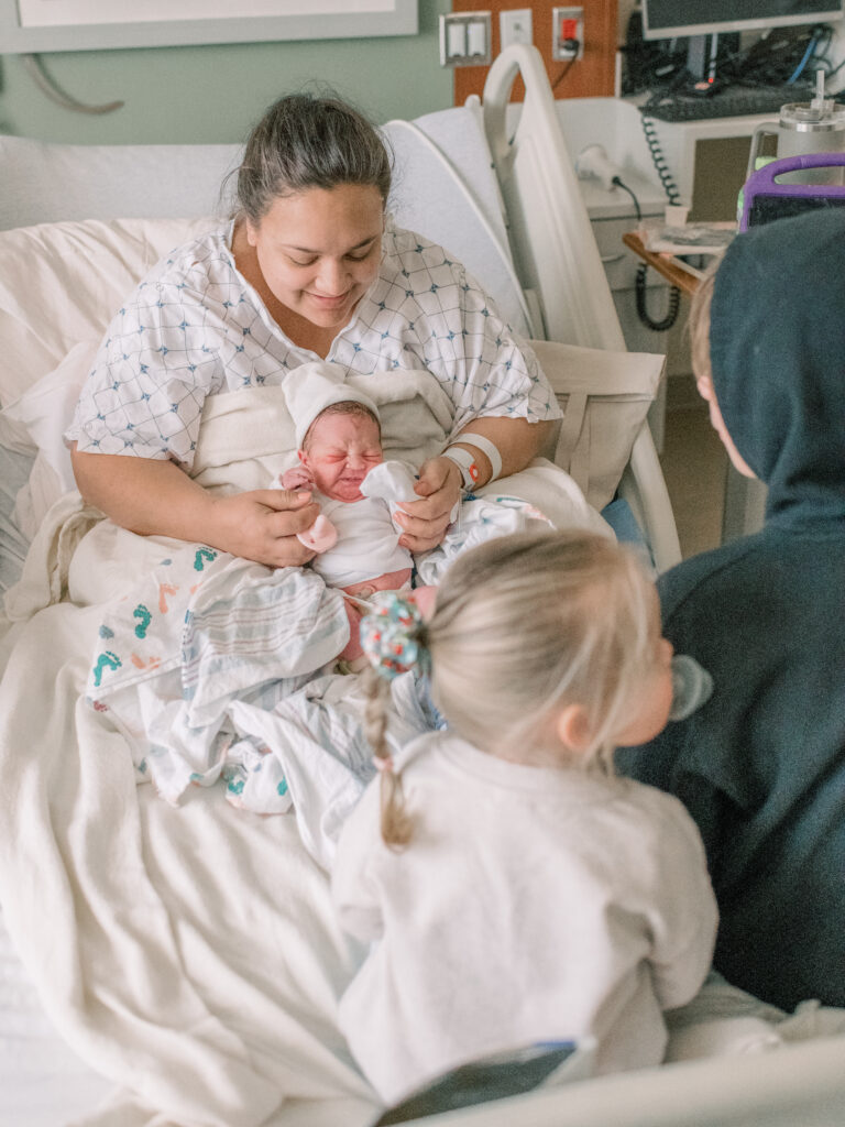 Brand new mom in hospital bed at Medstar St. Mary's Hospital after delivery with her three children.