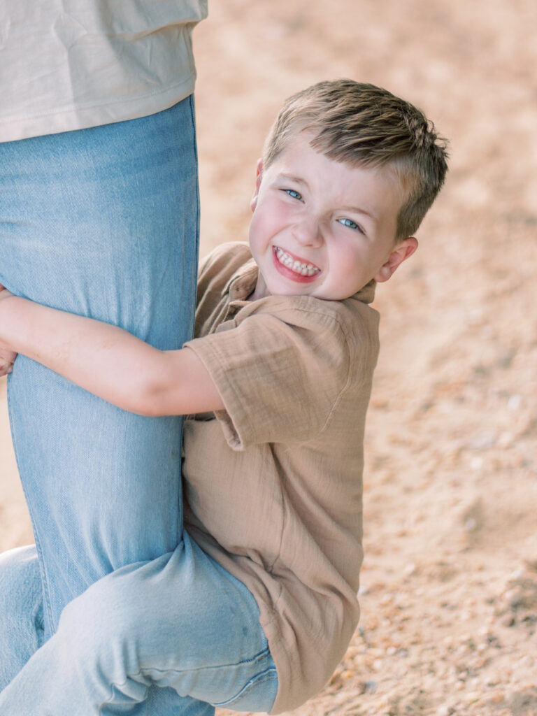 Young blue eyed boy holding onto his Dads leg.