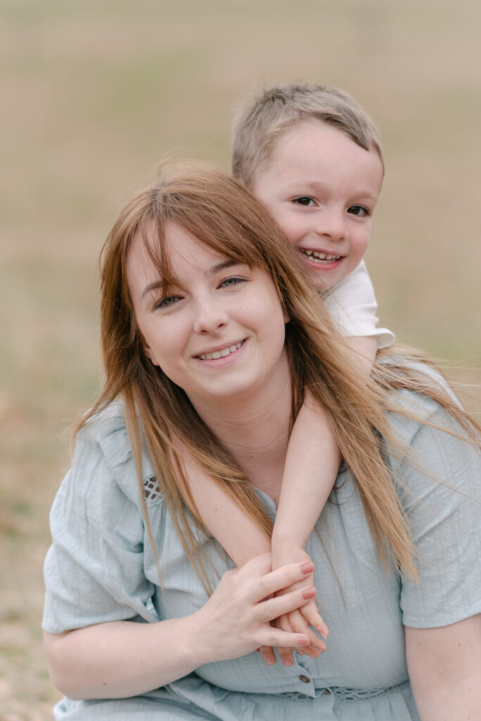 Brown haired boy with arms wrapped around his Moms neck.
