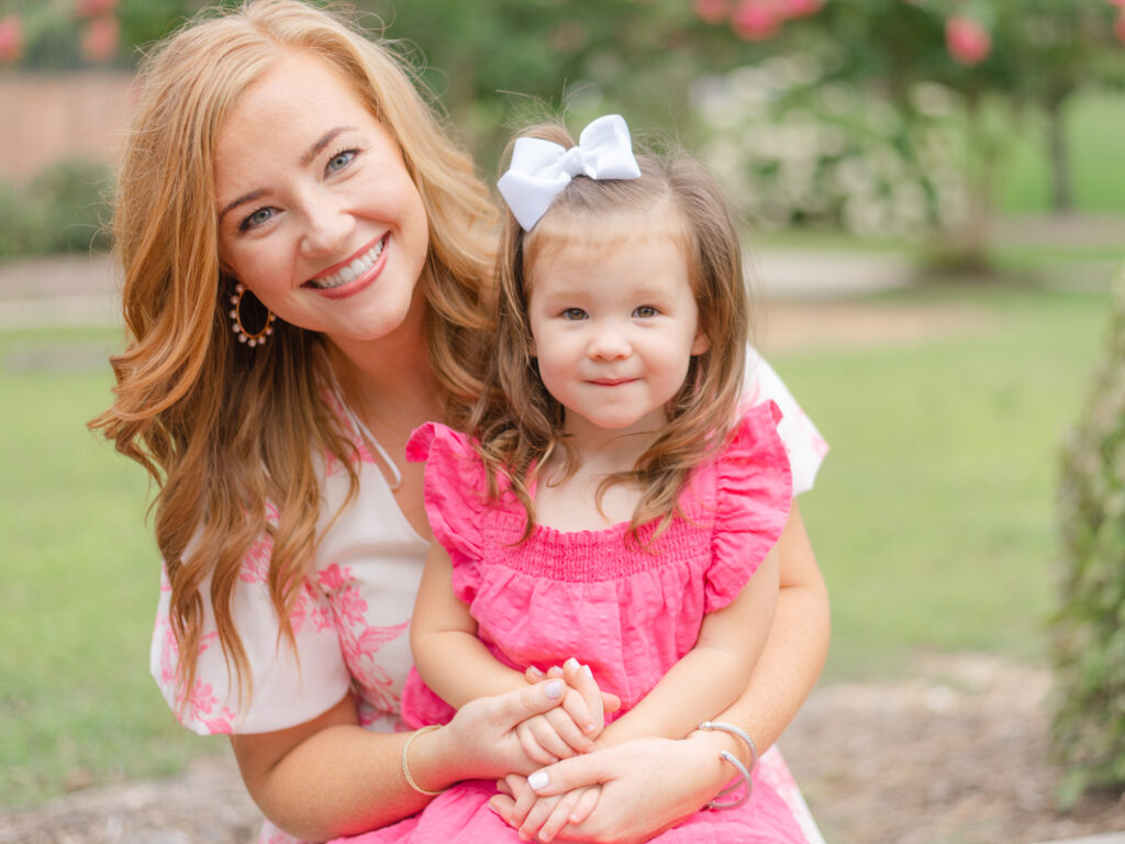 Beautiful red haired mom with young daughter wearing pink smiling at the camera.
