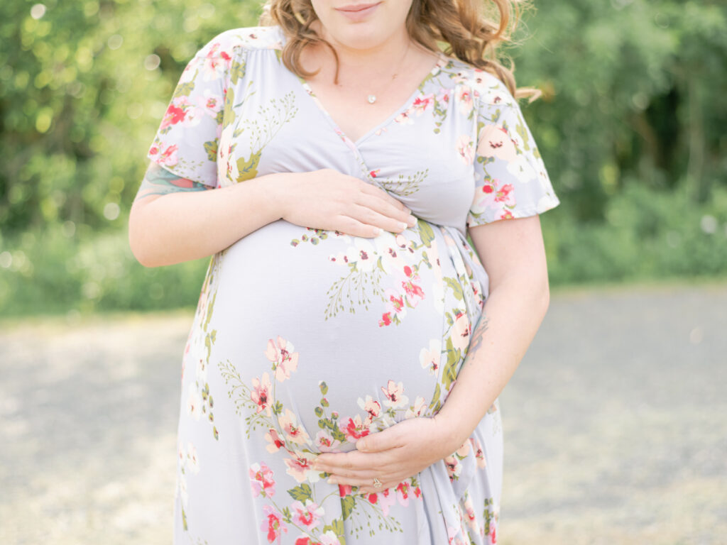 Pregnant mom in floral dress holding baby bump in Port Tobacco field. 
