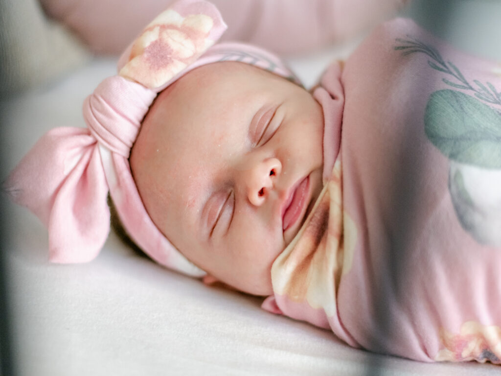 Baby girl wearing a pink floral bow laying in her black iron crib,