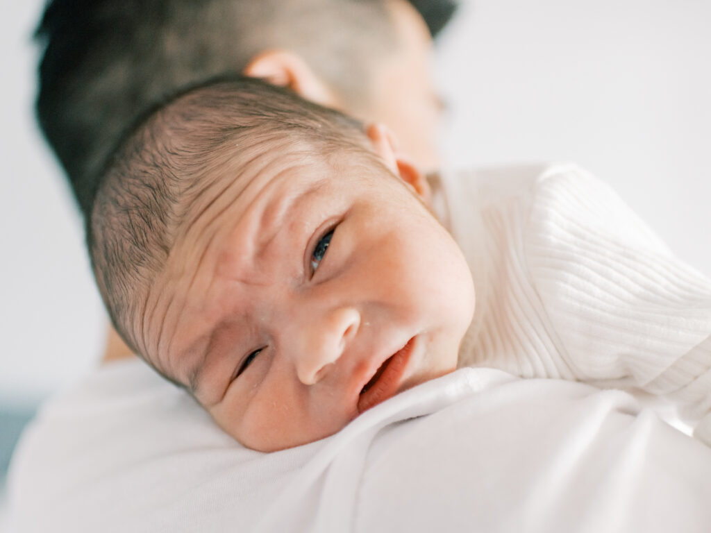 Newborn baby laying on his dads shoulder during a lifestyle newborn session with wrinkles on his forehead.