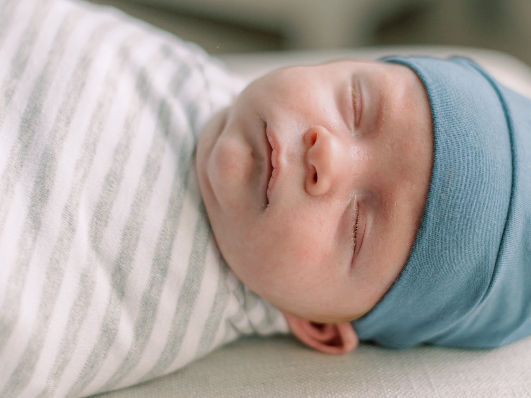 Newborn baby wrapped in gray stripped swaddle with blue hat on.