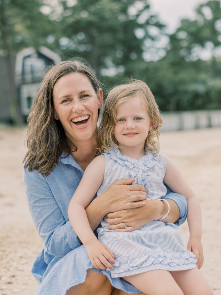 Mom during Richmond Mini Session wearing blue dress while on beach holding daughter in her lap.
