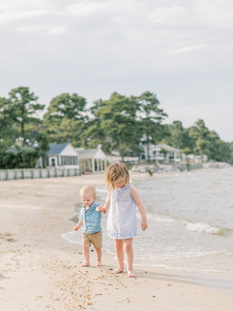 Young boy holding older sisters hand while walking on beach,.